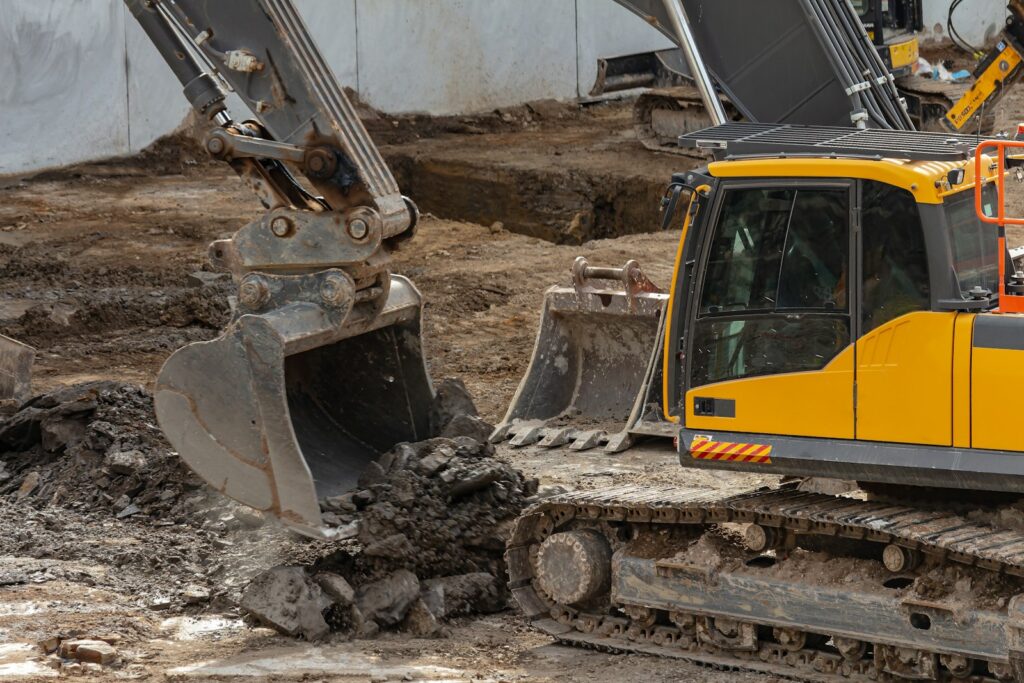 Yellow and black excavator on brown soil, the kind of machinery used to clear old land
