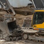 Yellow and black excavator on brown soil, the kind of machinery used to clear old land