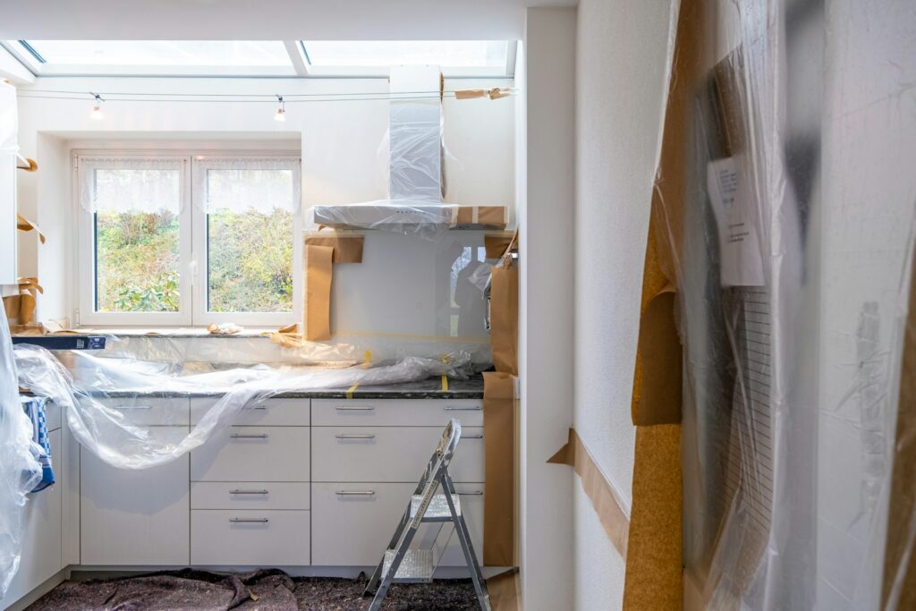 Kitchen under renovation with white cabinets covered in plastic and brown paper