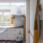 Kitchen under renovation with white cabinets covered in plastic and brown paper