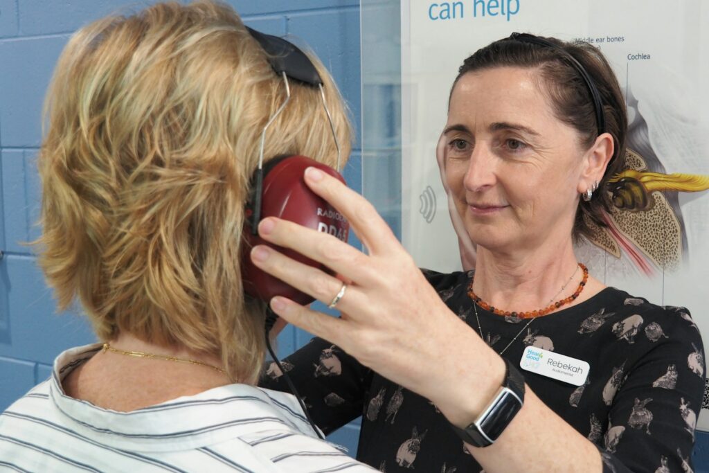 Audiologist placing headphones on a woman before a hearing test