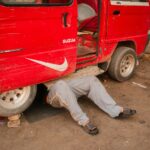 Person lying under a red van carrying out repairs, part of keeping a fleet running