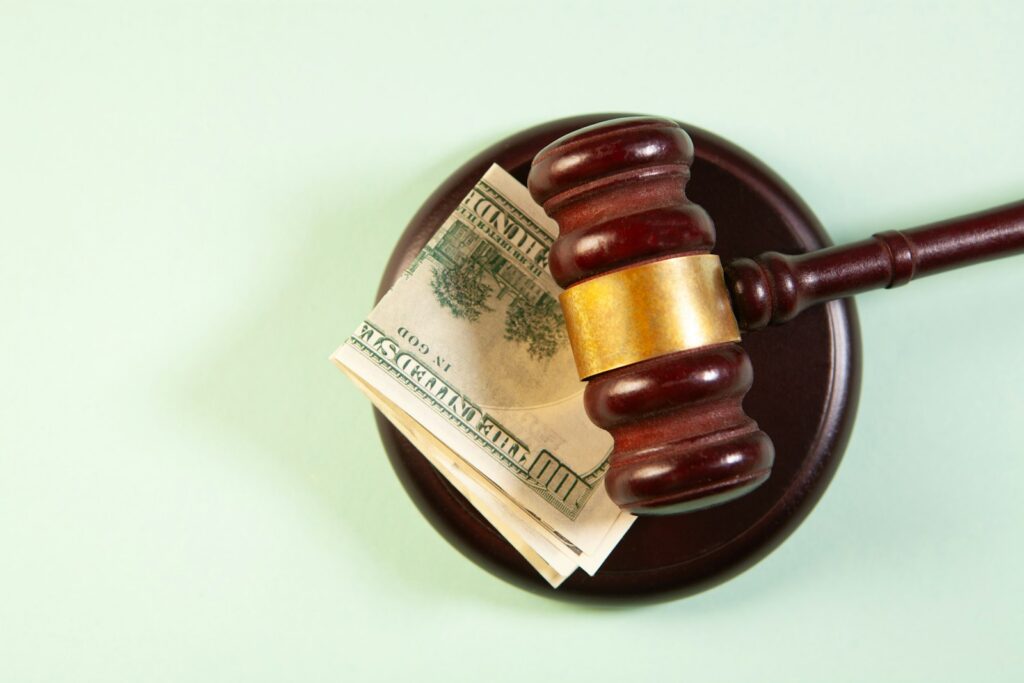 Wooden judge gavel on a sound block with money, suggesting the cost of litigation
