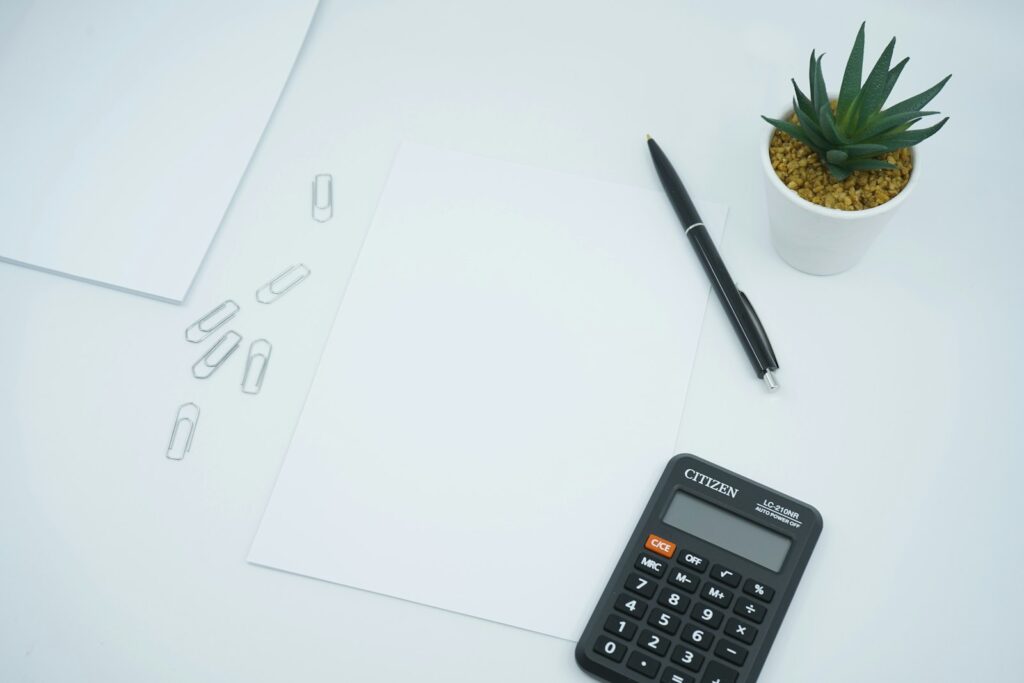 Black calculator beside a black pen on white paper on a desk, ready to crunch numbers
